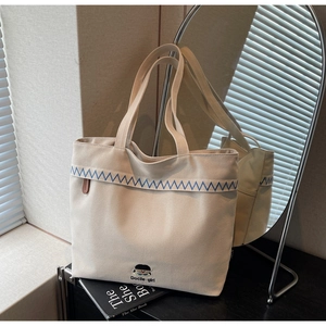 Close-up of beige canvas tote bag with blue wavy embroidery and Docile Girl cartoon logo