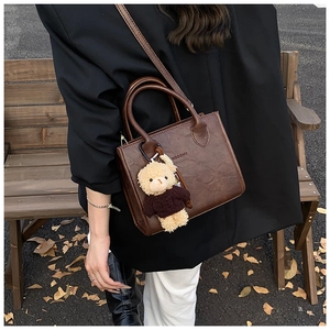 Detail of dark brown vintage faux leather crossbody bag with a plush bear pendant charm