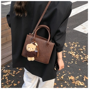 Close-up of vintage brown leather handbag with cute teddy bear charm in autumn street setting