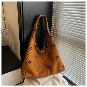 Detail of laser-cut flower pattern on brown suede tote bag with artistic lighting