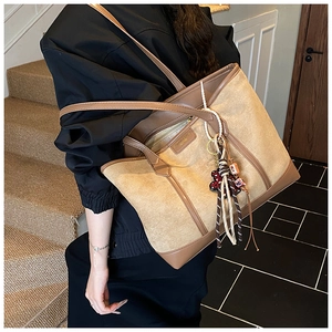 Detail of light brown tote bag with contrast leather trim and decorative tassel charms