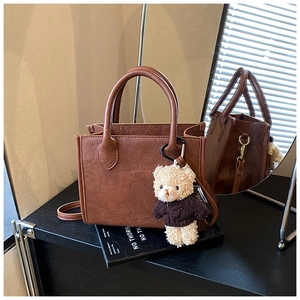 Detail of brown vintage small square bag with teddy bear charm and textured faux leather