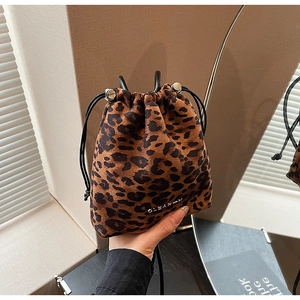 Détail du sac seau en daim léopard avec fermeture à cordon et logo métallique