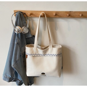 Detail of canvas tote bag with blue wavy embroidery and small Doodle-girl character print