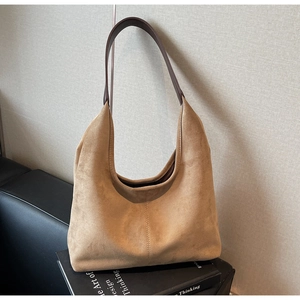 Detail of suede hobo shoulder bag in camel finish with brown leather strap on books