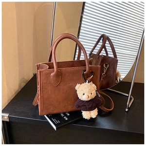 Detail of brown vintage handbag with embossed logo and cute plush bear charm