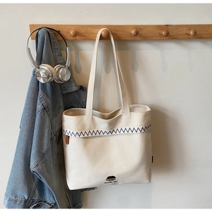 Detail of minimalist canvas tote bag featuring blue wave embroidery and handle hooks