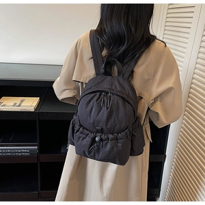 Detail of black nylon backpack featuring a drawstring closure worn with a beige trench coat