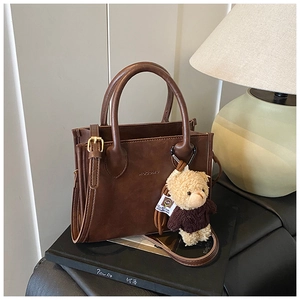 Detail of dark brown leather tote bag with brand logo and cute plush teddy bear charm