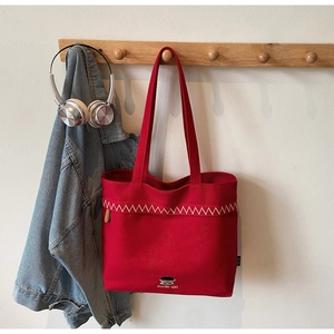 Detailed close-up of red canvas tote bag with white zigzag stitching and logo detail
