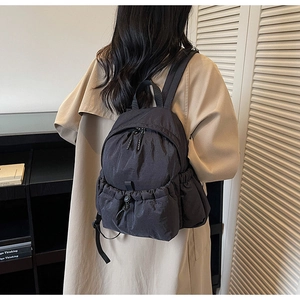 Back view of a casual black nylon backpack on a model showing size and fit in a room