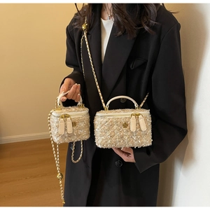 Detail view of two beige tweed mini box bags with gold camellia hardware and chain straps
