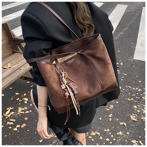 Dettaglio borsa tote in pelle scamosciata marrone con rifiniture in pelle e ciondolo etnico
