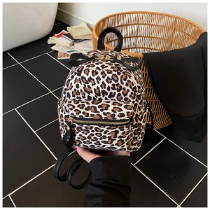 Detail of a mini leopard print backpack featuring black leather straps and zipper pockets