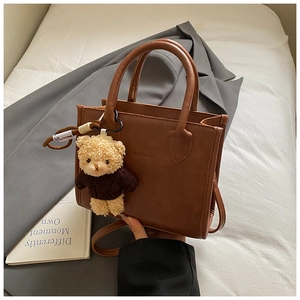 Detailed view of brown leather crossbody bag with a cute teddy bear charm pendant