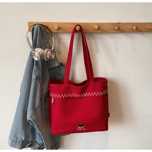 Detail of red canvas tote bag featuring white zigzag stitching and cartoon girl embroidery
