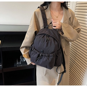 Detailed close-up of a black nylon backpack with a zipper pocket and side drawstring pocket