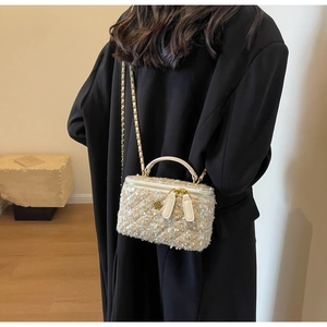 Detail of light gold tweed box bag featuring camellia logo and chain shoulder strap