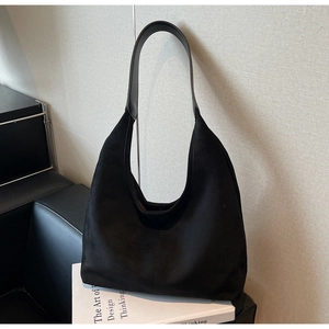 Detail of black suede hobo bag placed on a book against a minimalist grey background