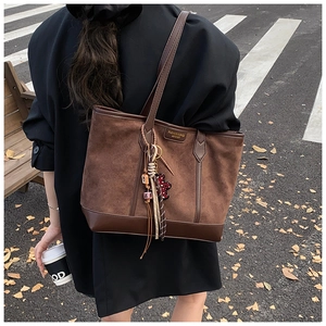 Detail of a vintage brown suede tote bag with fringe charm on a stylish autumn street
