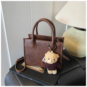 Detail of dark brown leather tote bag with lychee texture and cute teddy bear charm