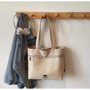 Close-up of beige canvas tote bag with blue wavy embroidery and long shoulder strap