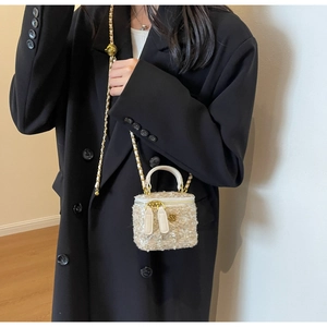 Close-up of white tweed box bag featuring golden chain strap and camellia metal pendant