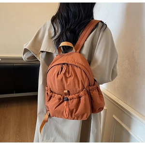 Rear view of model wearing a brown nylon backpack with drawstring pocket over a trench coat