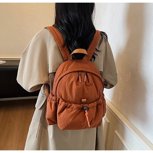 Detail of an orange lightweight canvas backpack with functional pockets on a female model