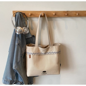 Close-up of beige canvas tote bag with blue zigzag embroidery and cartoon illustration