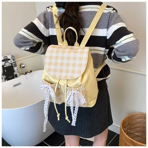Detail of yellow school backpack with plaid flap and white lace bow on the side pocket