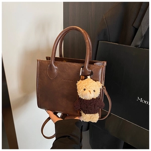 Close-up of a brown leather tote bag with HOGOMU logo and a cute teddy bear charm
