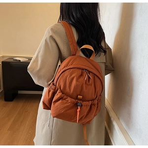 Close-up of burnt orange nylon backpack featuring drawstring pockets and side strap details