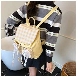 Dettaglio dello zaino giallo con fiocco in pizzo bianco e patta a quadretti moda
