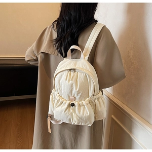Detail of a cream canvas backpack featuring a drawstring front pocket and side storage