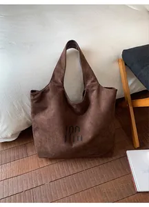 Detail of soft dark brown suede tote bag with black logo in a home setting
