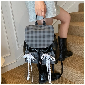 Detail of checkered patchwork backpack featuring large white lace bows and leather texture