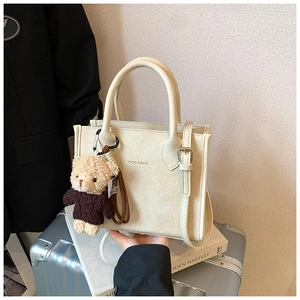 Detail of off-white structured handbag with a brown teddy bear charm on a suit background