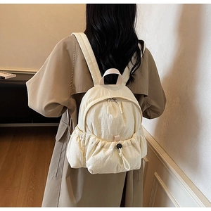 Rear view of a model wearing a beige nylon backpack in a bright minimalist setting