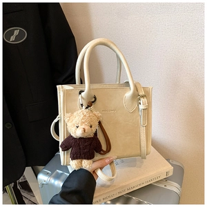 Detail view of a beige faux leather mini tote bag with an adorable brown teddy bear charm
