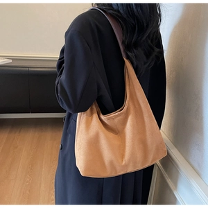 Brown suede tote bag shown on shoulder featuring wide strap and matte texture detail