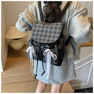 Detail view of plaid patchwork backpack with decorative white lace bows on black leather
