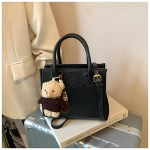Detail of black pebbled leather handbag with SOCOMU logo and brown bear plush charm