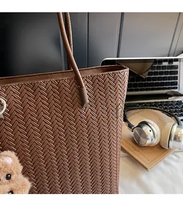 Detail of dark brown woven tote bag featuring a plush bear pendant and textured pattern