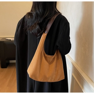 Detail of tan suede hobo bag with deep brown leather strap worn over a black coat