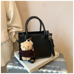 Detail of black leather handbag with BOGOMU logo, crossbody strap and cute bear charm