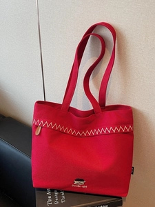 Red canvas tote bag with Docile-girl embroidery and white wavy stitching on a book