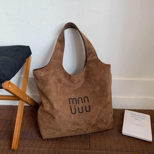 Detailed view of brown suede tote bag with black logo on a minimalist background
