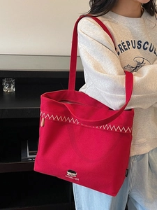 Red canvas tote bag with cartoon embroidery and shoulder strap shown in lifestyle scene