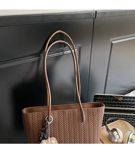 Close-up of brown woven tote bag with plush pom-pom charm and slender shoulder strap detail